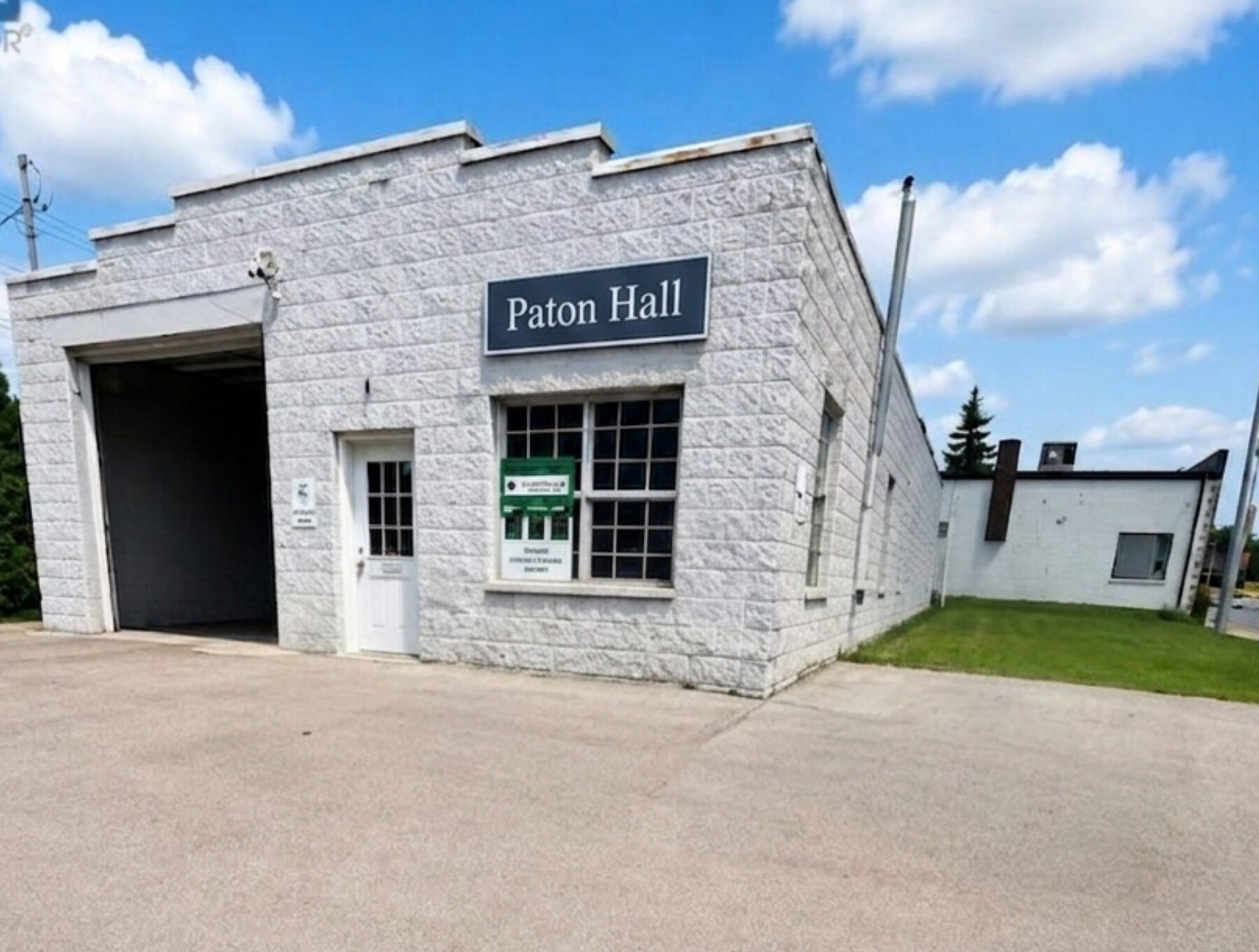 The front of Paton Hall: a single-storey
      rock-faced concrete block building with an open garage bay and a dark navy
      sign reading Paton Hall.