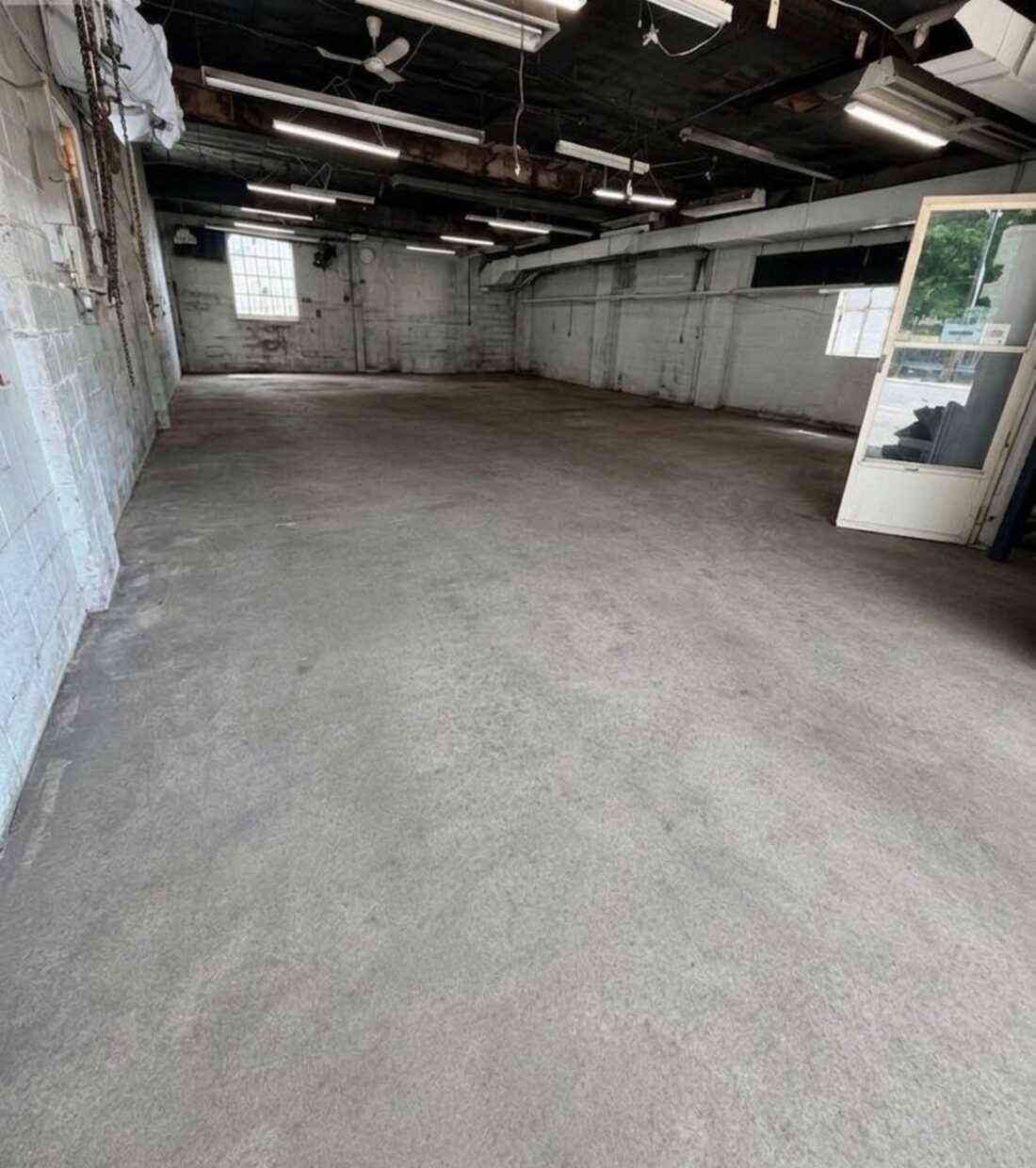 The interior: a long open concrete
          floor, black-painted ceiling with exposed joists and fluorescent strip
          lights, painted block walls.