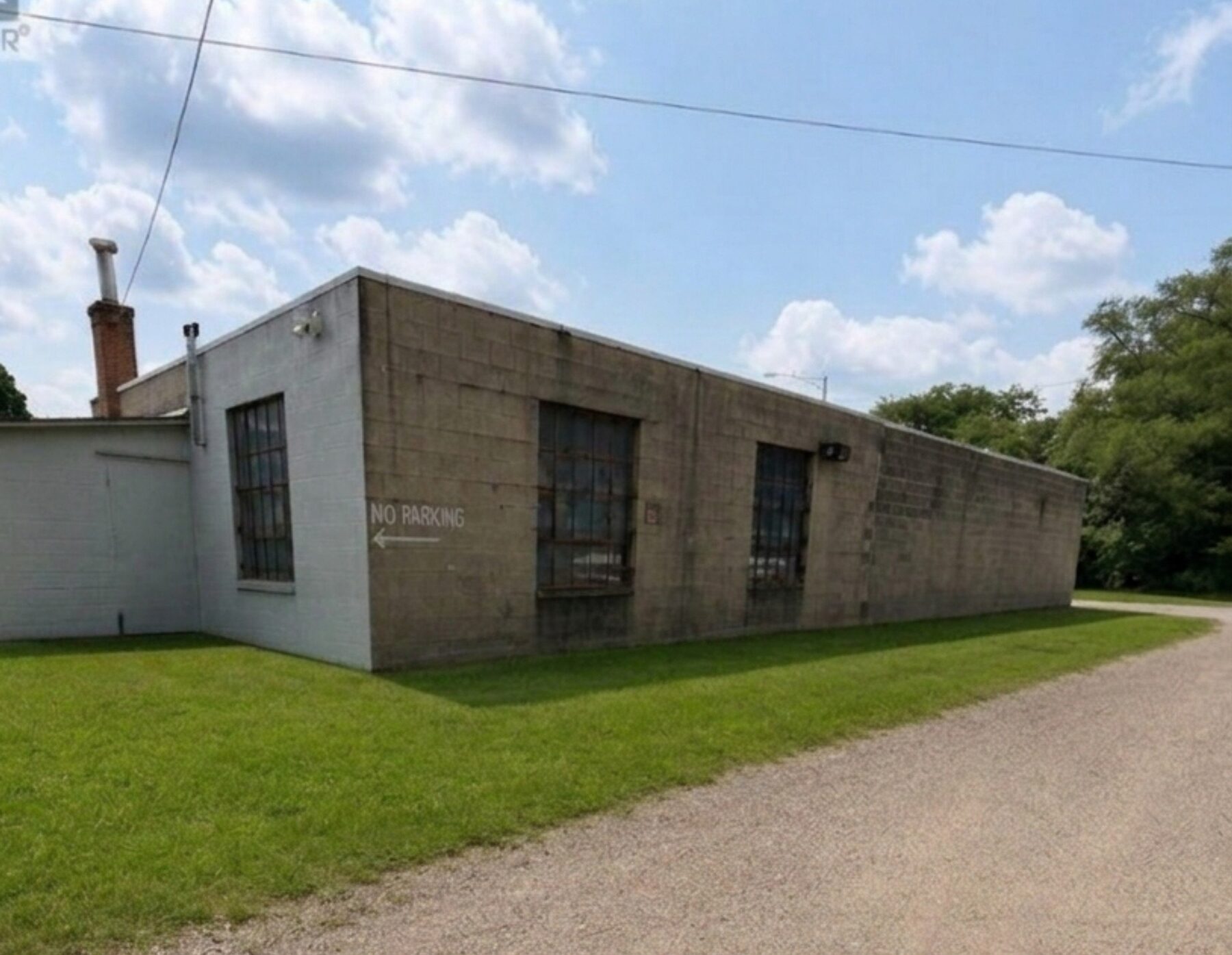 The long side of the building in
        painted concrete block, with tall steel-frame industrial windows and a
        gravel drive.